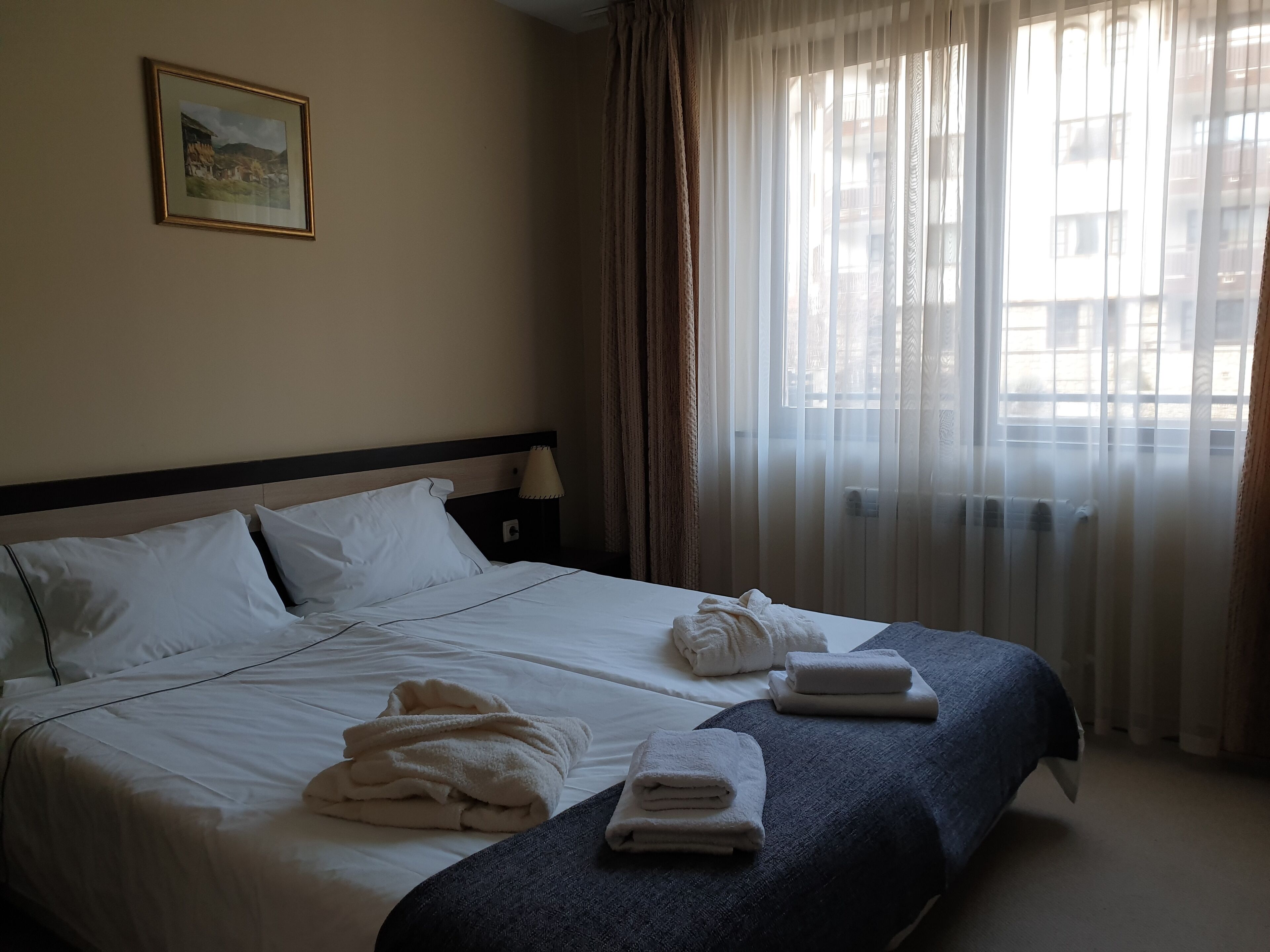 Quarto de hotel com cama bem arrumada, um quadro na parede e janela com cortinas leves.
