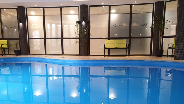 Piscina interior com água azul cristalina, rodeada por paredes de vidro com janelas jateadas.