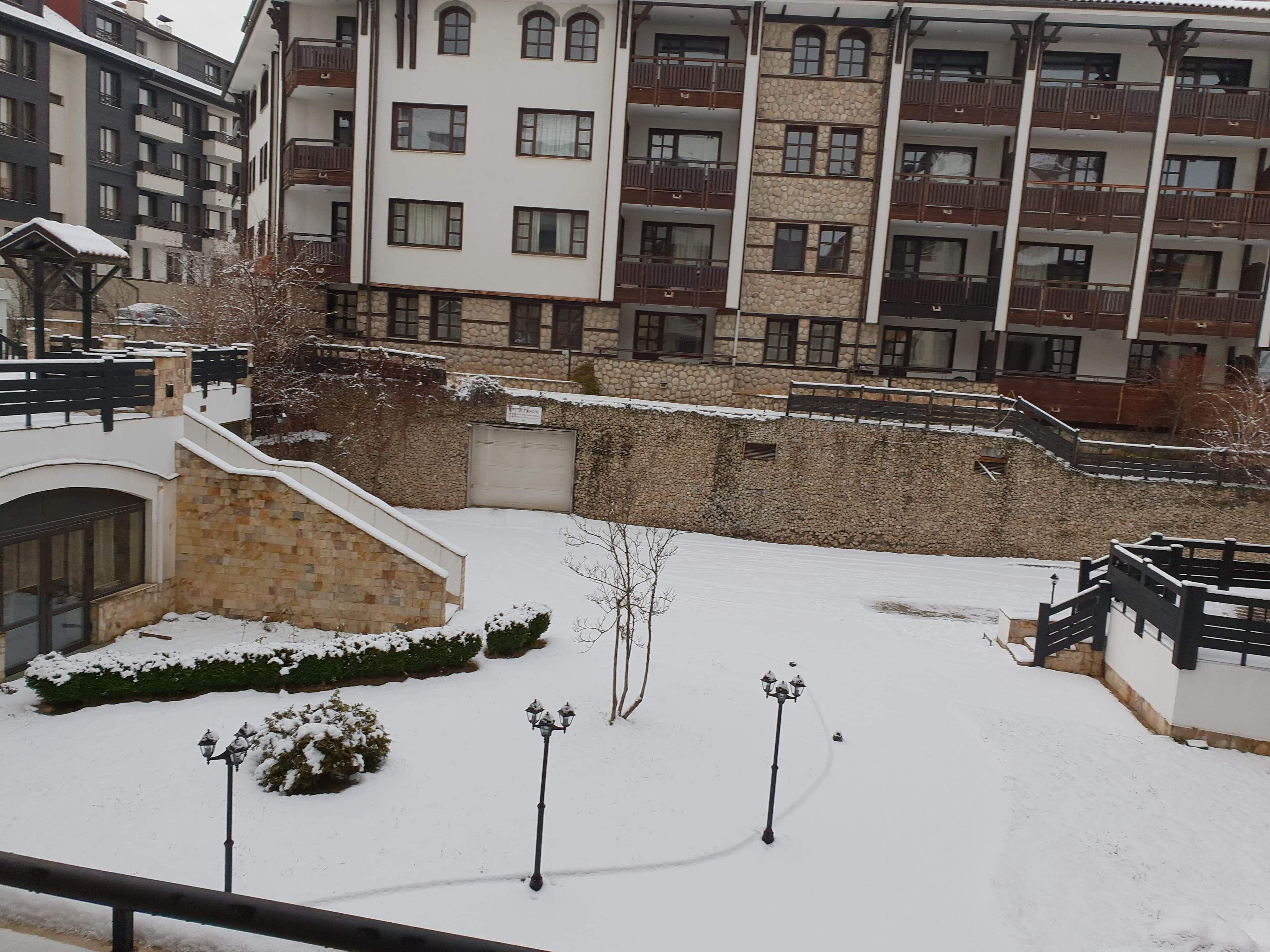 Ein verschneiter Innenhof mit einer Steinmauer, einer kleinen Brücke und einem Gebäude mit mehreren Balkonen.