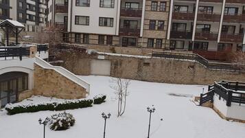 Ein verschneiter Innenhof mit einer Steinmauer, einer kleinen Brücke und einem Gebäude mit mehreren Balkonen.