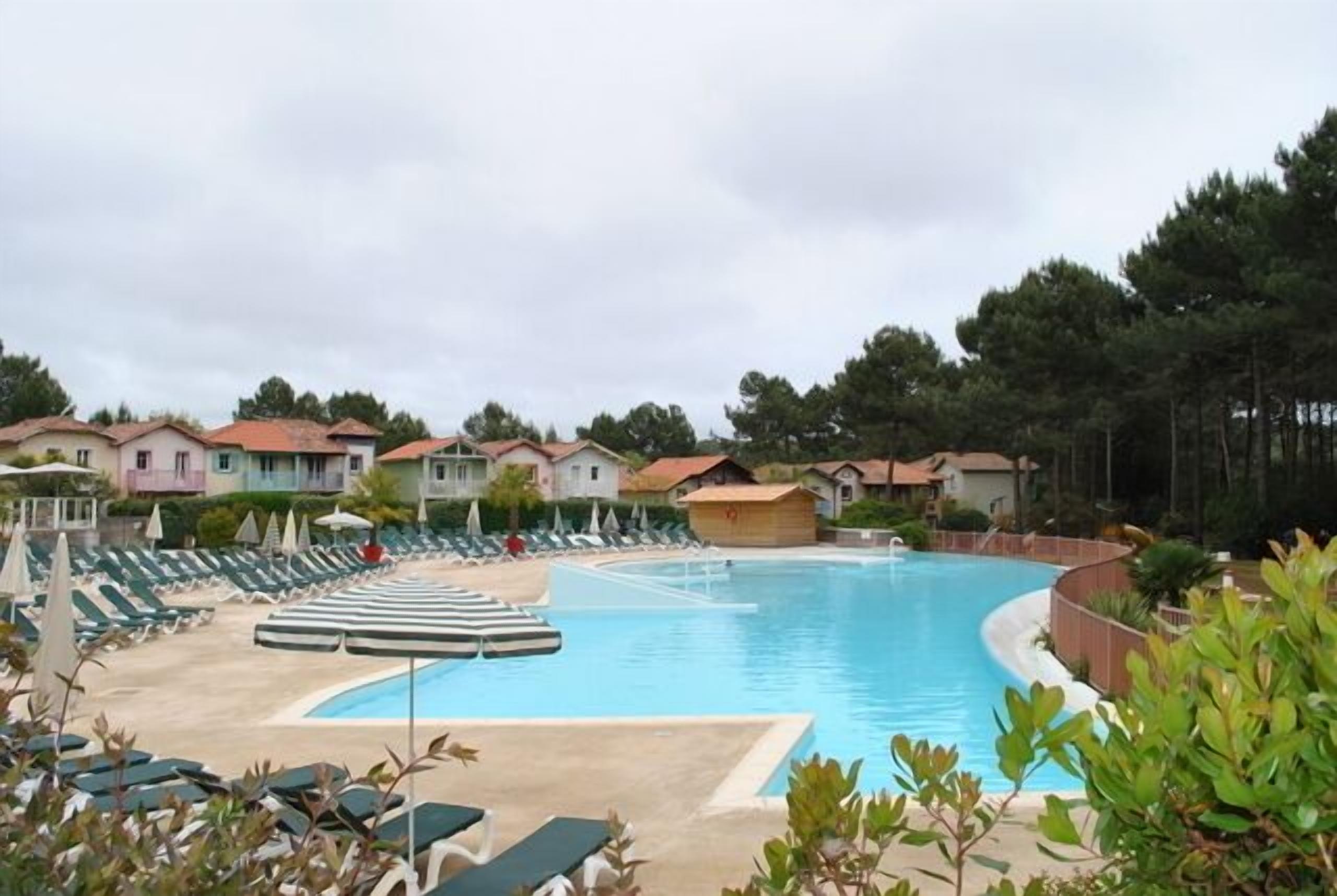 Ein Swimmingpool mit Liegestühlen und Sonnenschirmen, umgeben von Häusern und Bäumen.