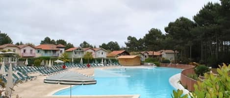 A swimming pool with lounge chairs and umbrellas, surrounded by houses and trees.