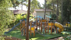 A playground with slides and climbing structures, surrounded by trees and a building in the background.