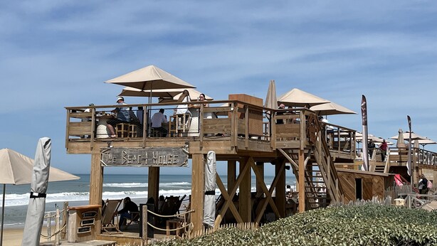 A wooden beach house with multiple levels, outdoor seating, and umbrellas.