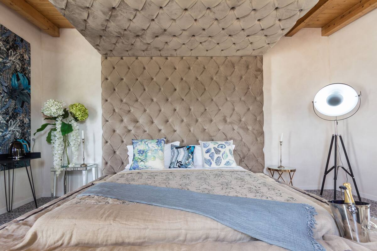 A bedroom with a tufted headboard, a bed with patterned bedding, a bedside table with a lamp, and a floor lamp.