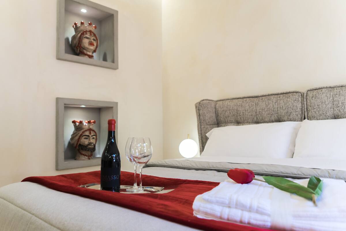 A hotel room with a bed, a red tray with a wine bottle and glass, and two decorative items on the wall.