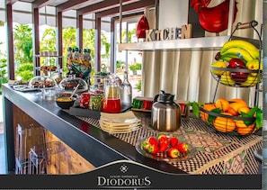 Un buffet proposant divers plats, une cafetière et un panier de fruits.