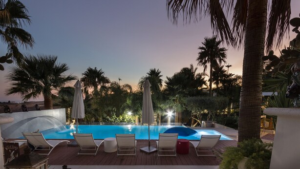 A pool area with lounge chairs and umbrellas, surrounded by palm trees and a sunset view. - Diodorus Luxury Experience (Favara)