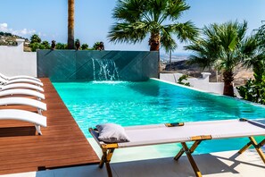 A pool with a waterfall feature, surrounded by palm trees and lounge chairs. - Diodorus Luxury Experience (Favara)