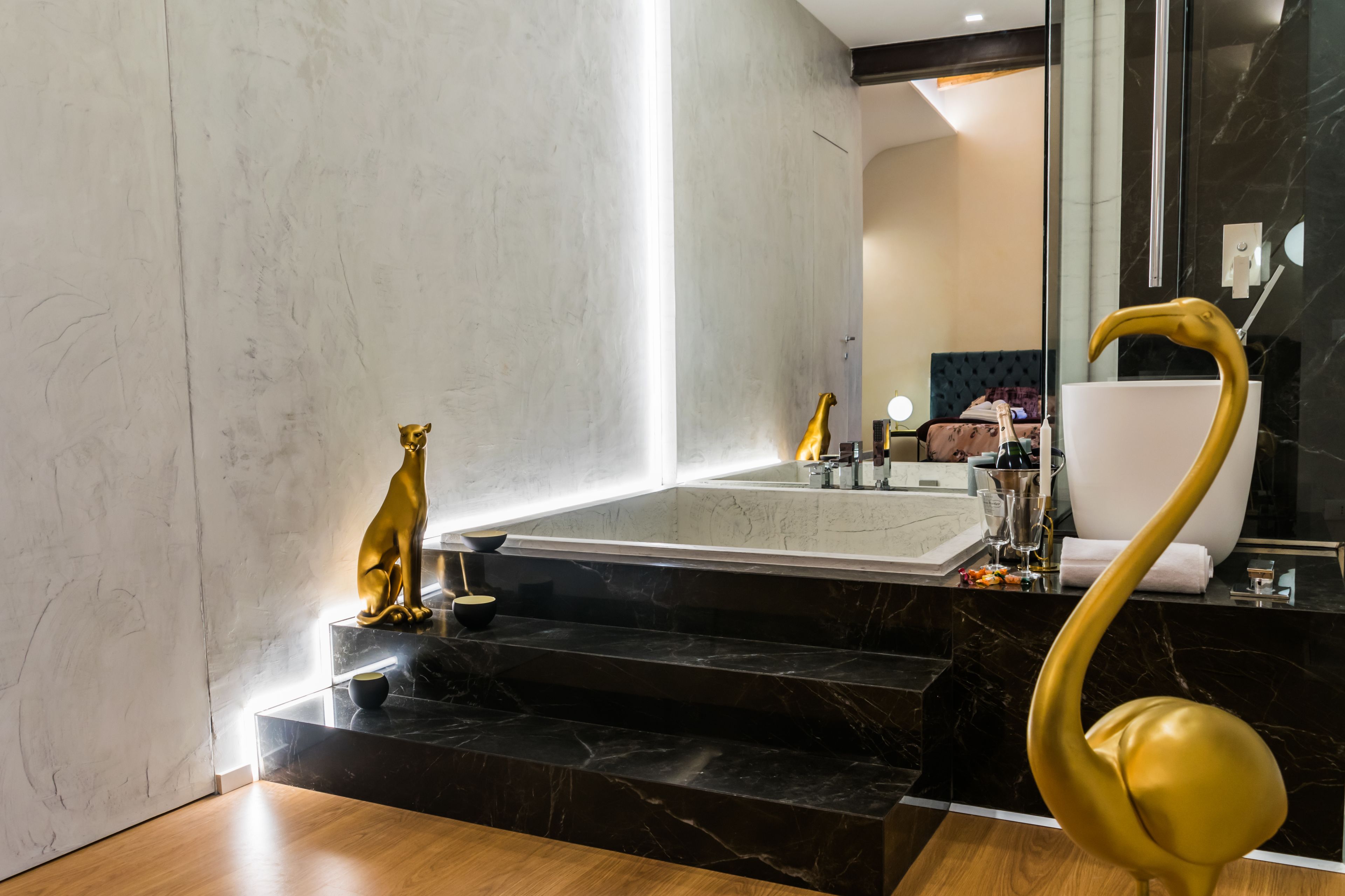 Un baño moderno con un lavabo de mármol, una estatua dorada y un espejo curvo singular.