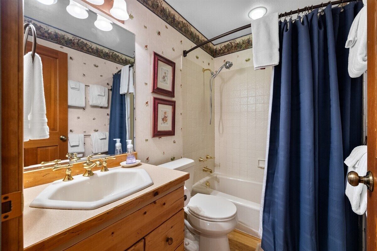 Un bagno con lavandino, water e doccia. Asciugamani appesi al muro e tenda da doccia.