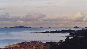 Une vue côtière avec des bâtiments sur une colline, une mer calme et des îles au loin.