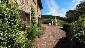 A stone building with a brick pathway leading to an outdoor seating area with a table and chairs. - Lilium, splendid villa with outdoor space, on the hills of San Giminiano (San Gimignano)