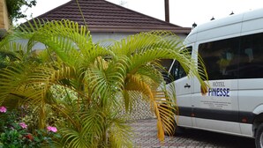 A white van with "HOTEL FINESSE" branding parked in front of a building with a tiled roof. - Hotel Finesse (Kinshasa)
