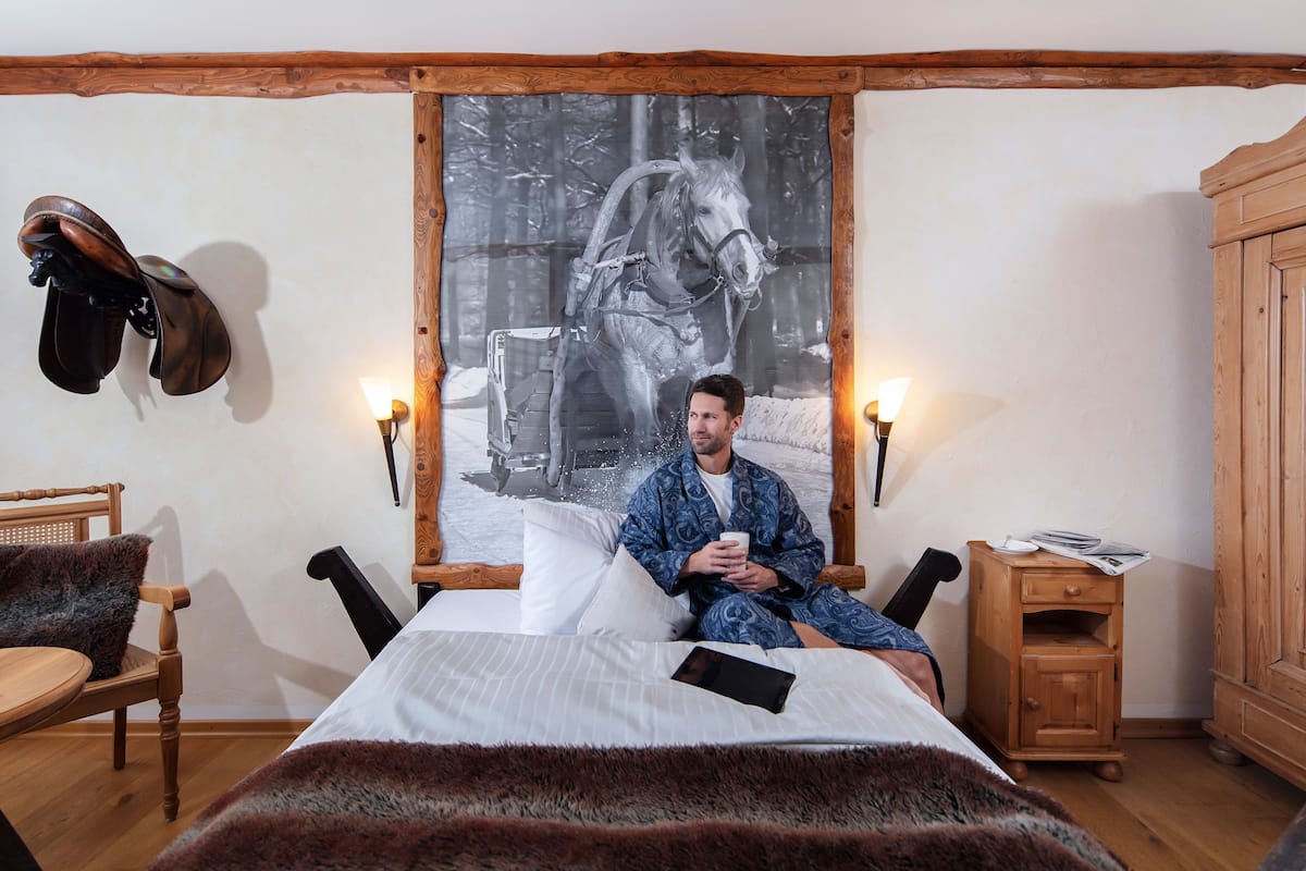 A room with a bed, a chair, a wooden cabinet, and a wall-mounted coat rack.