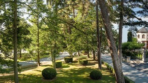 A large, historic house with a prominent tower, surrounded by a well-maintained garden and a paved driveway.