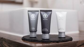 Three toiletries on a wooden tray in a bathroom with a bathtub and a mirror.
