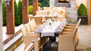 An outdoor dining area with wicker furniture, stone walls, and a view through an arched doorway.
