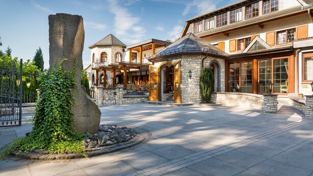 A spacious courtyard with a stone fountain, a large tree, and a stone wall.