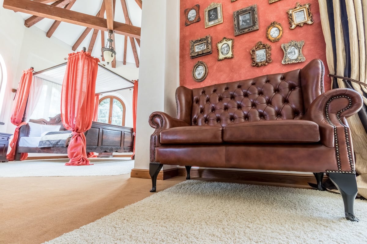 A room with a brown leather sofa, a red curtain, and a wall adorned with framed pictures.