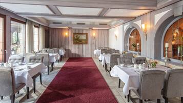 A formal dining room with tables set for service, a red carpet, and a painting on the wall.
