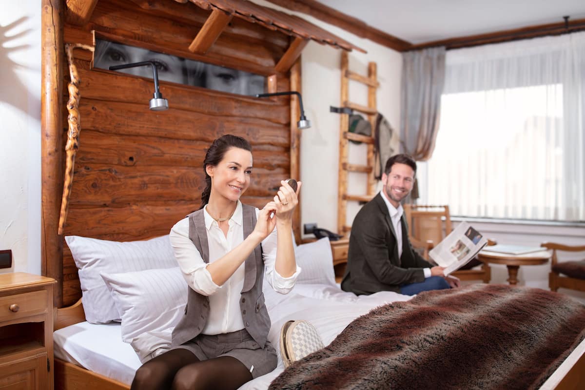 A wooden cabin-style bedroom with a bed, a wooden headboard, a nightstand, a lamp, and a window with curtains.
