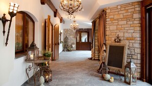 A hallway with a stone wall, wooden beams, a chandelier, and a framed mirror.
