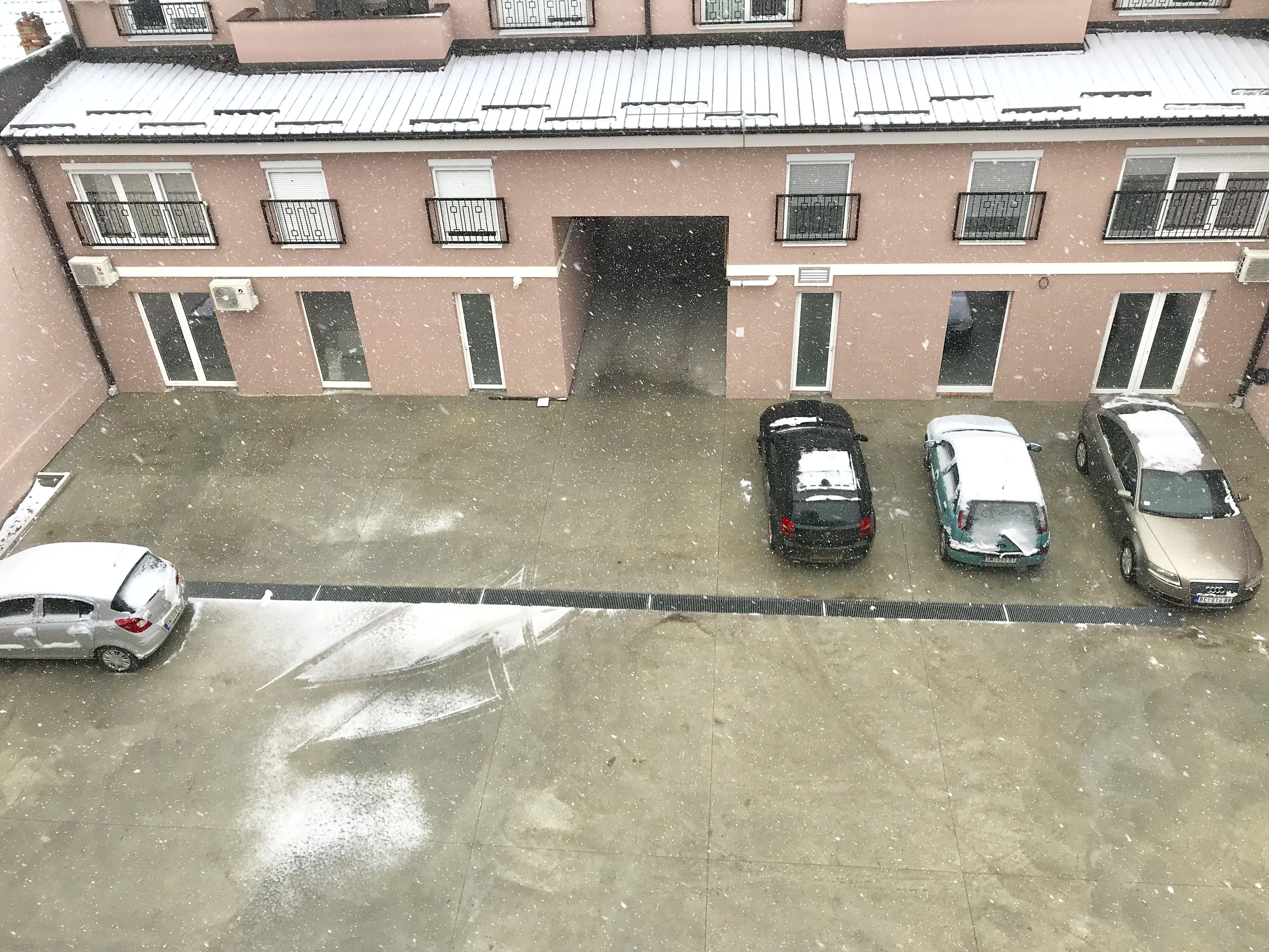 A parking lot with several cars and a building with a tiled roof and multiple windows.