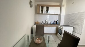 A compact kitchen with white cabinets, a microwave, and a stove. There's a glass dining table with a clear bowl and two chairs.