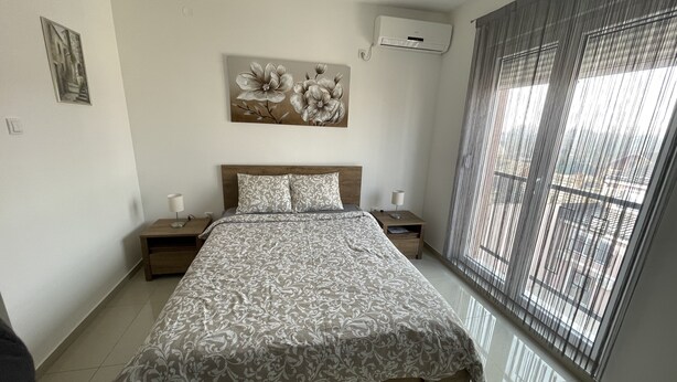 A bedroom with a bed, nightstands, a wall-mounted air conditioner, and a window with blinds.