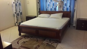 A bedroom with a wooden bed, white bedding, a patterned rug, and a nightstand. - Shikara Apartment (Mombasa)