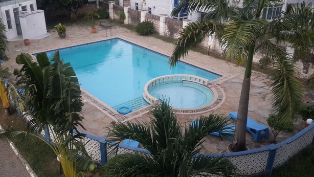 A rectangular pool with a circular hot tub, surrounded by a stone deck and palm trees. - Shikara Apartment (Mombasa)