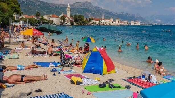 A crowded beach with people sunbathing and swimming, a colorful tent, and a historic building in the background.