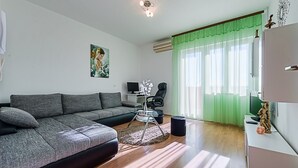 A modern living room with a grey sectional sofa, a small round table, a TV, and a green curtain.