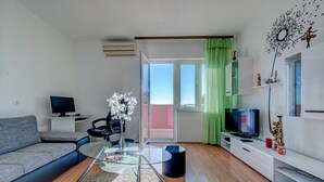 A modern living room with a sofa, a glass coffee table, a TV, and a balcony with green curtains.