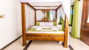 Een hemelbed met een baldakijn, groen beddengoed en witte kussens.
