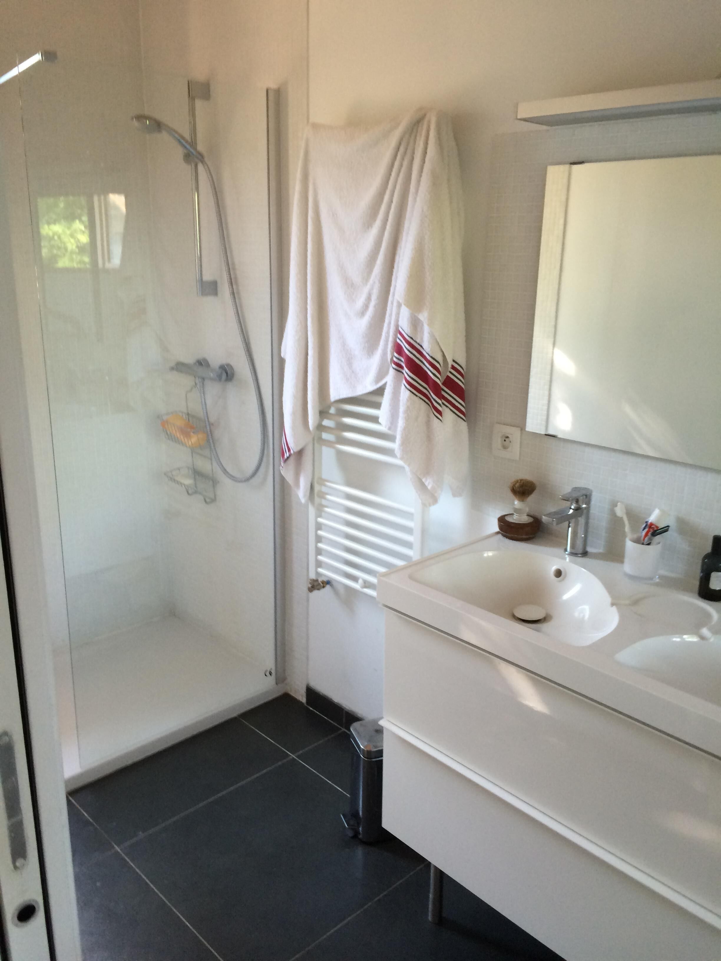 A bathroom with a glass-enclosed shower, a white sink with a mirror, and a towel rack with a towel.
