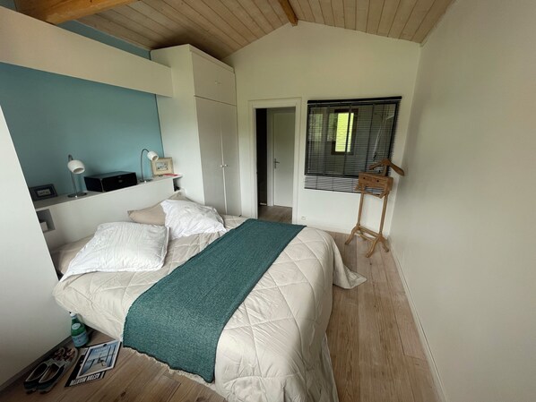 Une chambre à coucher avec un lit, une table de chevet avec une lampe, un cintre en bois et une fenêtre avec des stores.