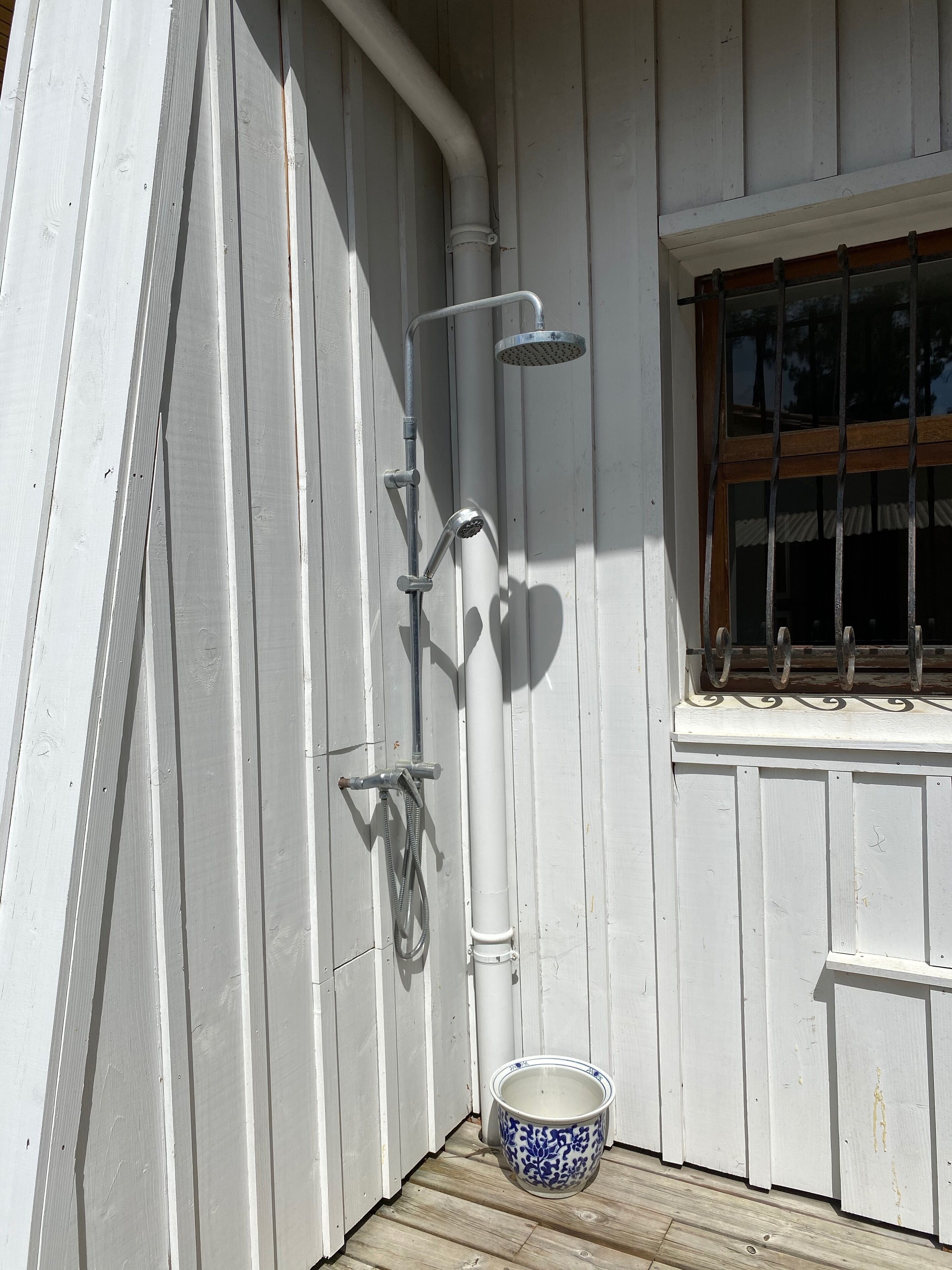 Fachada de madera blanca con ventana y cabezal de ducha metálico.