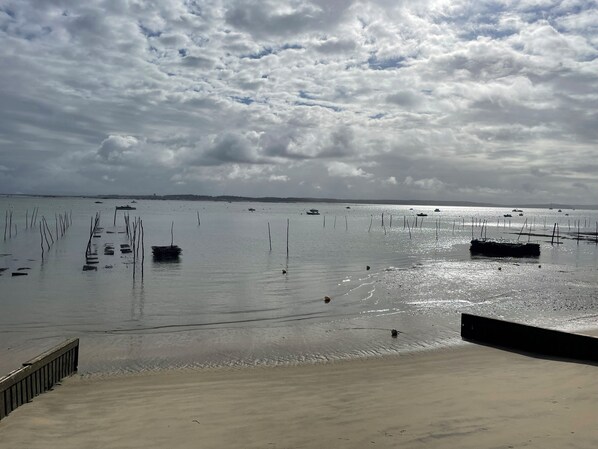 A beach with a wooden walkway leading to the water, boats in the distance, and a cloudy sky.