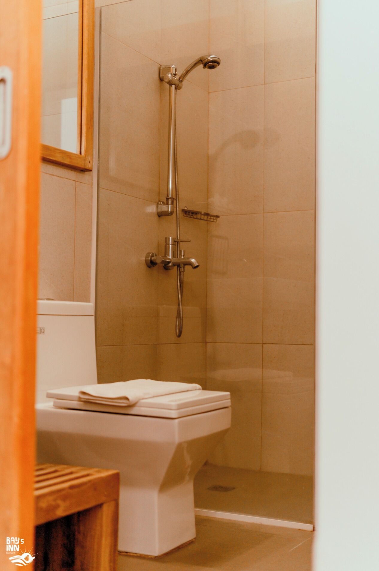 Un baño con ducha, inodoro y un taburete de madera.