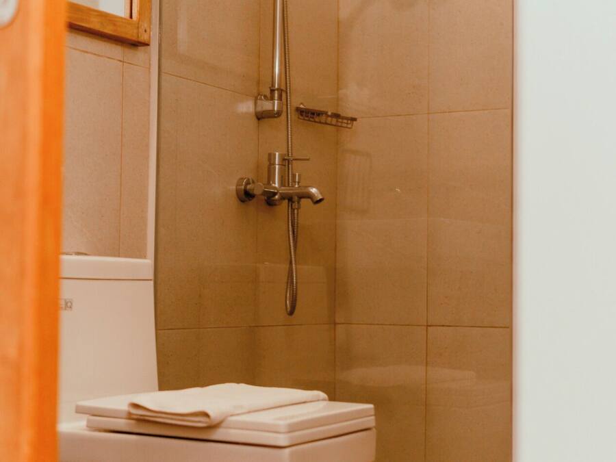 Un baño con ducha, inodoro y un taburete de madera.