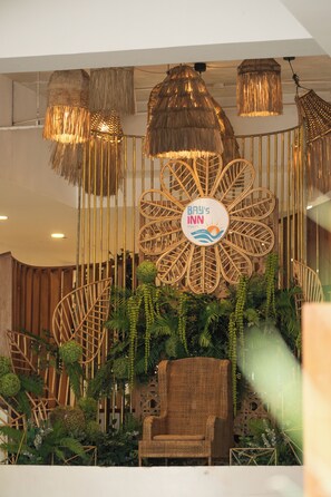 A lobby area with a central decorative structure, a wicker chair, and hanging lamps.