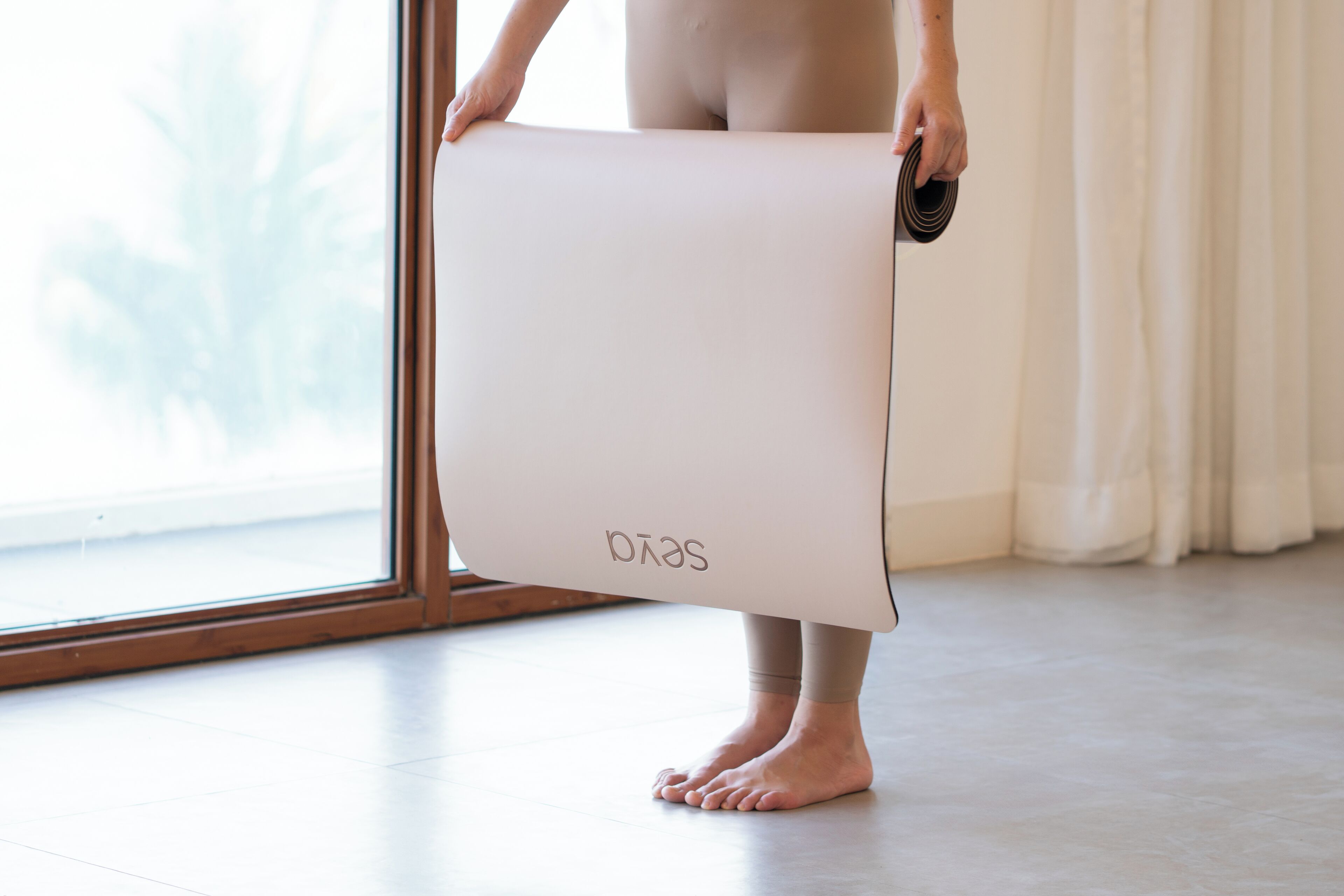 Una persona sosteniendo una colchoneta de yoga blanca, con el nombre de la marca a la vista.