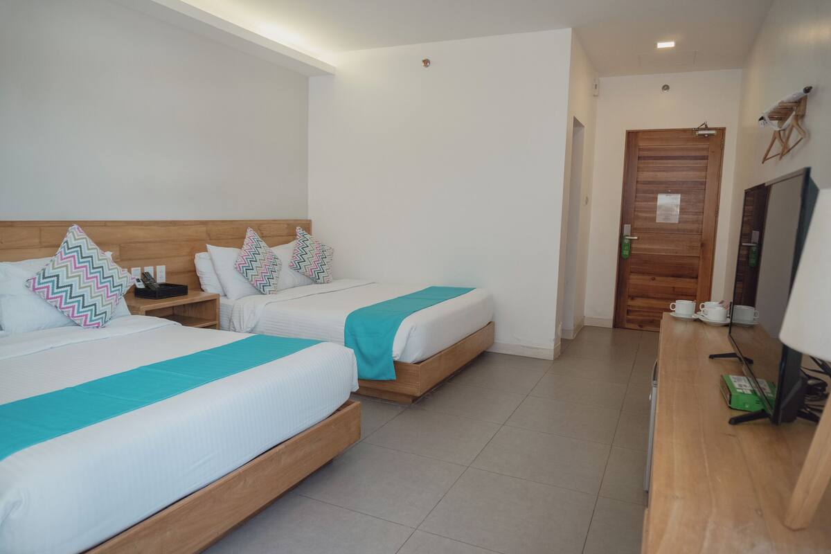 Ein Hotelzimmer mit zwei Betten, einem Holzkopfende, einem Schreibtisch mit Stuhl und einem Fernseher.