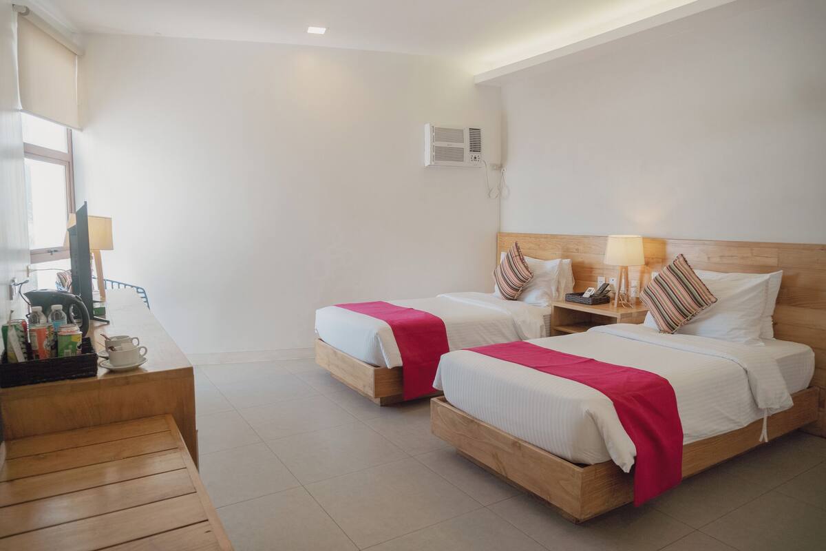Ein Hotelzimmer mit zwei Betten, Holz-Kopfteilen, Nachttischen mit Lampen und einer kleinen Sitzecke mit einer Bank.