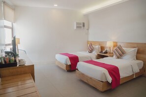 Habitación de hotel con dos camas, cabeceros de madera, mesitas de noche con lámparas y una pequeña zona de estar con un banco.