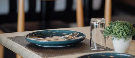 Una mesa de comedor preparada con platos, cubiertos, un vaso y una pequeña planta en maceta.