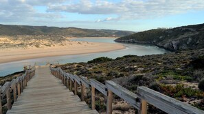 A wooden boardwalk leading to a beach with a view of the ocean and hills in the background.