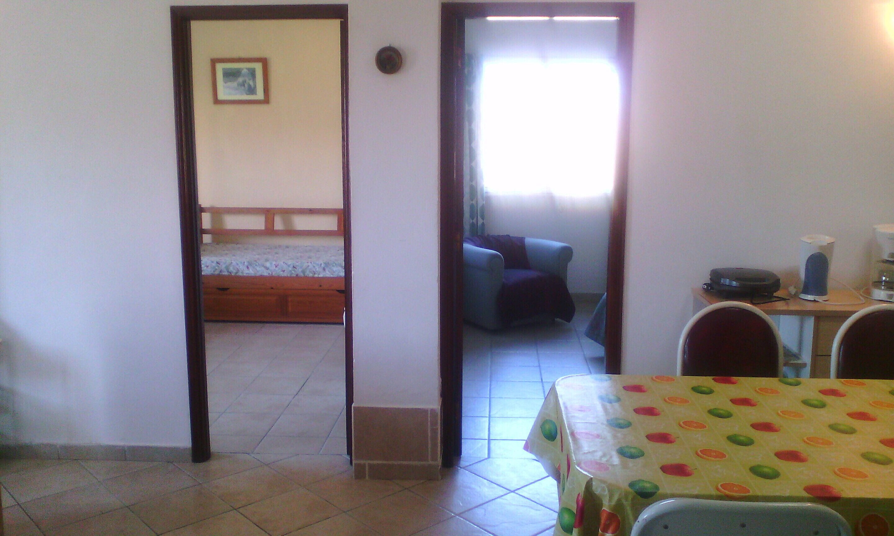 Une pièce comprenant un lit, un bureau et une chaise. Il y a une fenêtre avec des rideaux, un radiateur et une table recouverte d’une nappe à motifs.